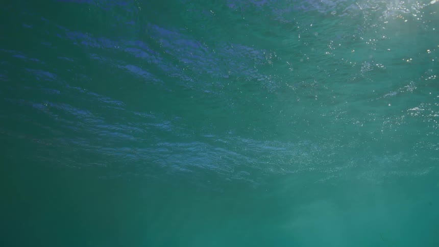 A serene underwater perspective captures the sunlight filtering through the gently rippling surface of the turquoise ocean