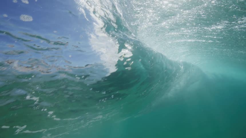Ethereal underwater view of a turquoise ocean wave curling and breaking in super slow motion
