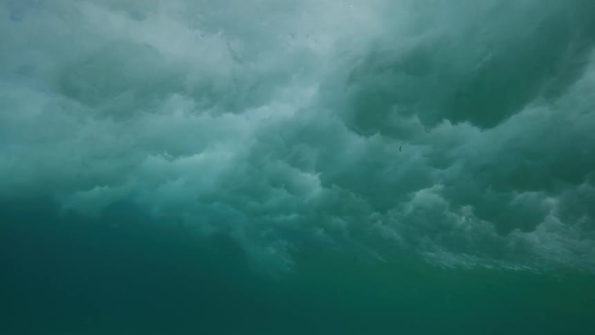 An underwater perspective of a large ocean wave breaking in ultra slow motion, creating a cloud of white water and bubbles