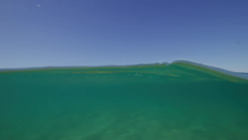 A serene slow-motion split view of the calm ocean surface from below and the clear blue sky above
