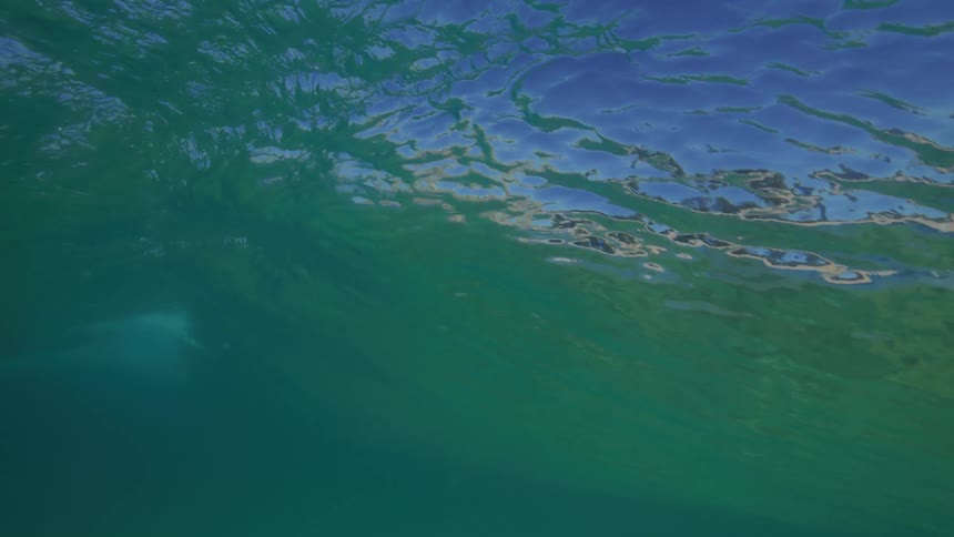 Slow motion underwater view from inside the barrel of a teal-colored ocean wave as it breaks