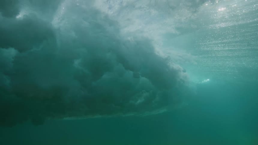 An incredible underwater slow-motion view of a powerful ocean wave crashing overhead as sunlight streams through the turquoise water
