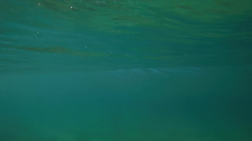 Looking up at the shimmering surface of the ocean from beneath the waves in slow motion