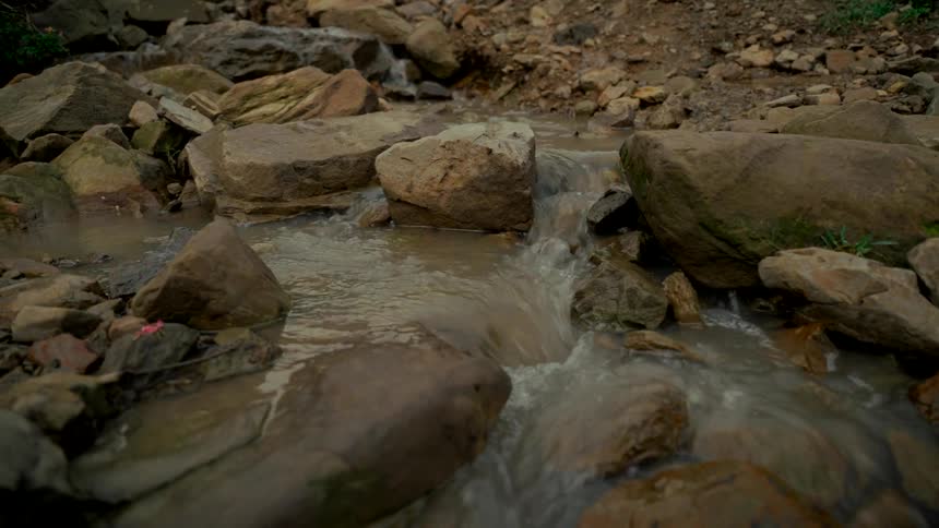 Water gently cascades over stones in a peaceful, shallow, and rocky stream bed