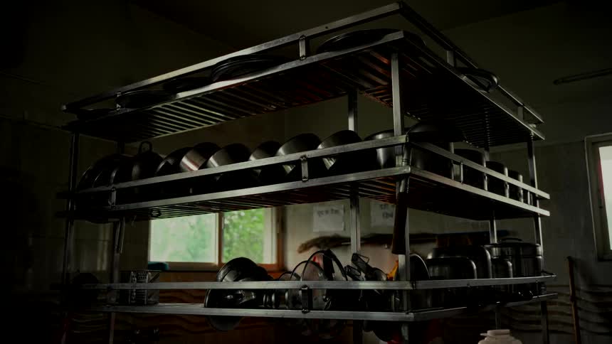 A low angle shot of a metal kitchen rack filled with pots and pans in a dimly lit commercial kitchen