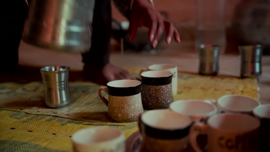 A person pours hot chai from a stainless steel pitcher into a rustic ceramic mug in slow motion