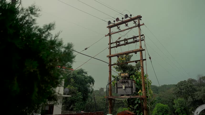 An electricity transformer on a wooden utility pole stands against a dark, stormy sky in a rural setting