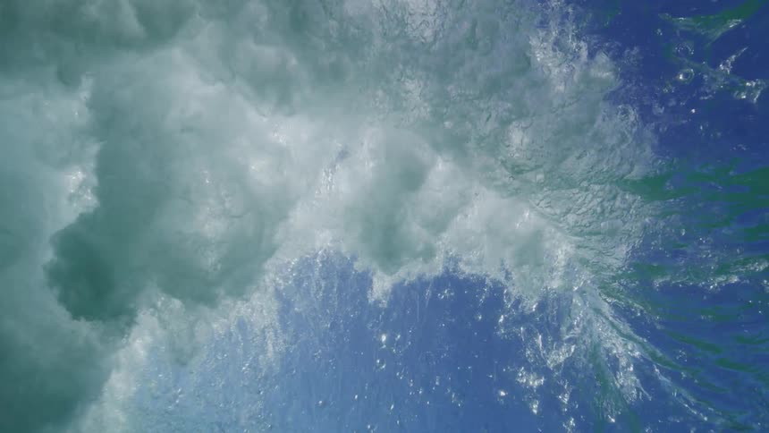 A stunning slow-motion underwater view as a powerful ocean wave crashes overhead, captured from below the surface