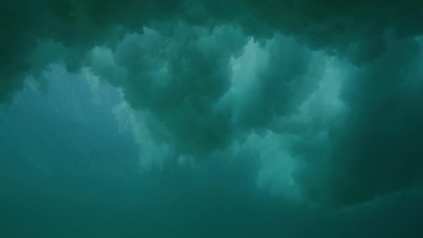 A slow-motion underwater view shows a powerful wave passing overhead, creating a turbulent cloud of bubbles and foam