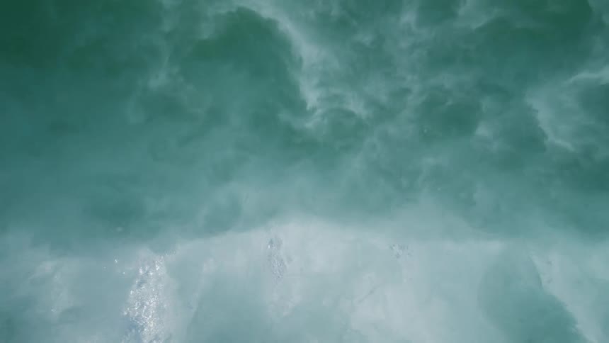 An upward-facing underwater view shows a tranquil sea surface before a large wave crashes overhead in slow motion