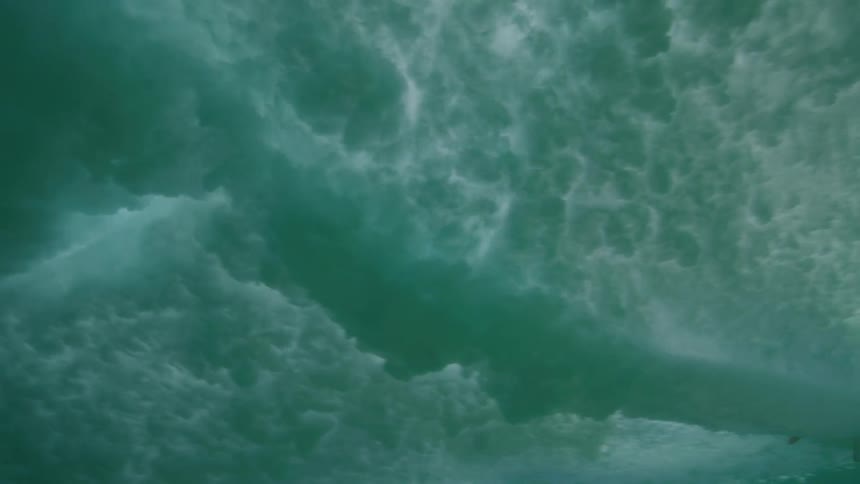 An immersive underwater slow-motion view captures a surfer on a longboard gliding across a crystal clear turquoise wave