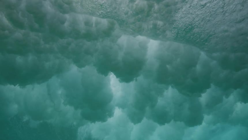 A mesmerizing underwater slow-motion view as a powerful ocean wave crashes overhead, creating a turbulent cloud of white water