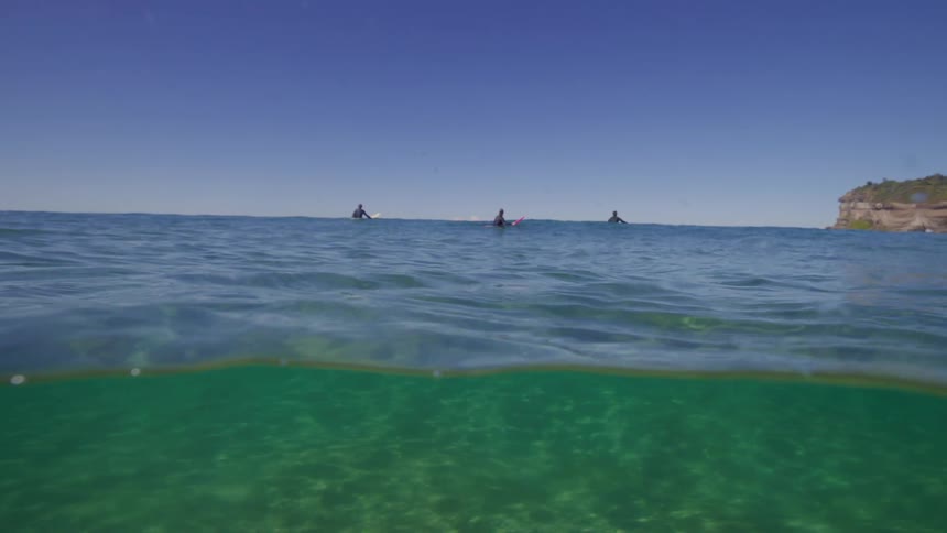 A serene split-level underwater view of the ocean reveals surfers waiting for waves on a calm, sunny day
