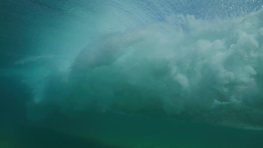 A stunning underwater slow-motion shot captures a powerful ocean wave as it forms and breaks, creating a beautiful and turbulent cloud of white water