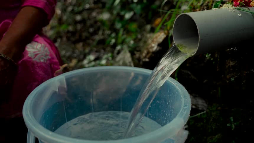 Close up of fresh spring water flowing from a PVC pipe into a plastic bucket