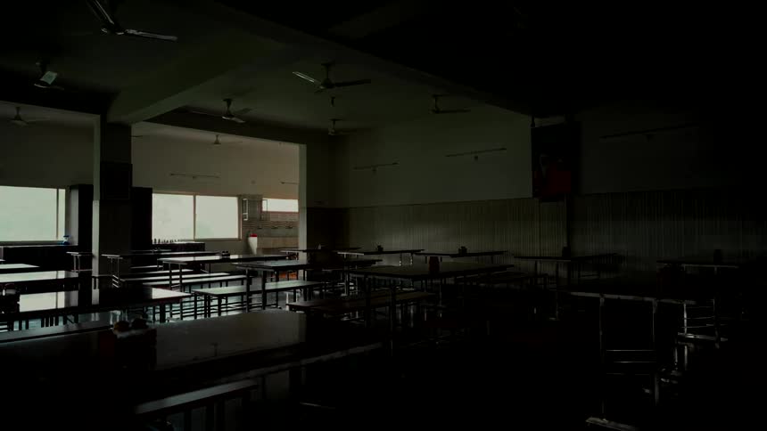 A wide, static shot of a dark and desolate institutional cafeteria with empty tables and benches