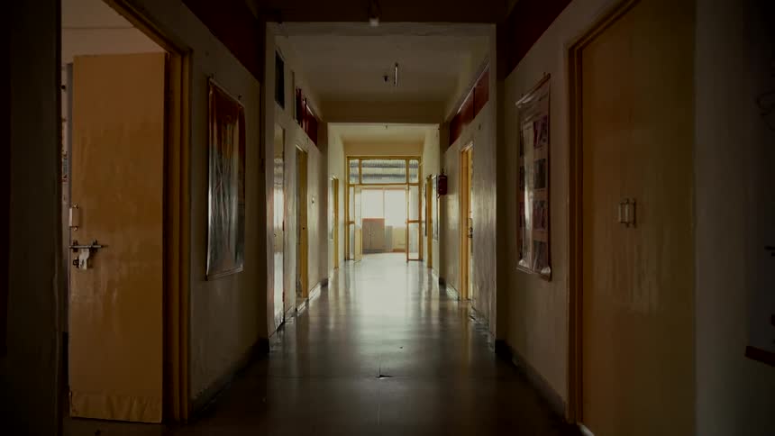 A static shot of a long, eerie, and empty hallway with dim lighting creating a suspenseful atmosphere