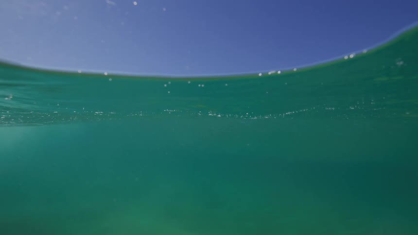 An immersive over-under shot captures a tranquil ocean wave slowly building and washing over the camera on a beautiful sunny day