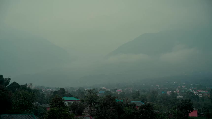 A scenic view of a mountain valley town enveloped in a thick, serene fog on an overcast day