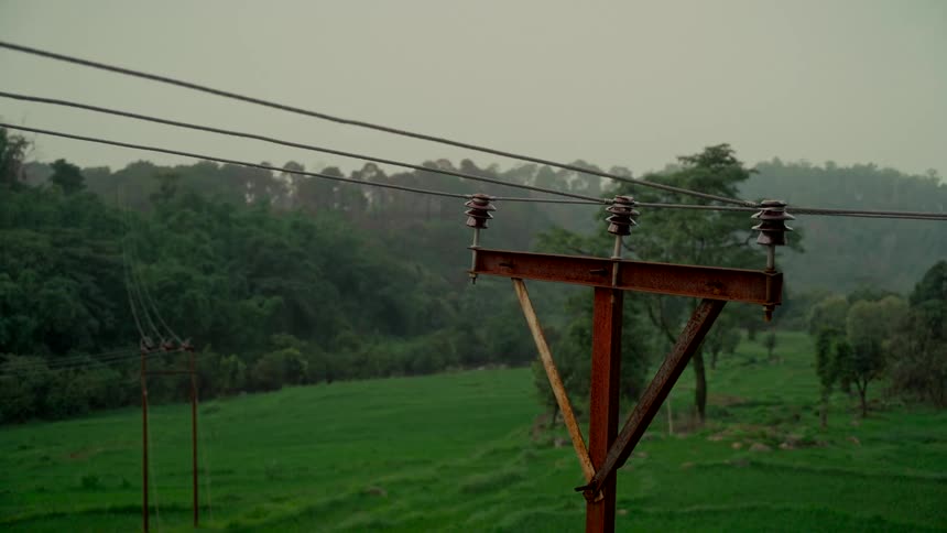 A weathered electrical pole with power lines stands in a lush green valley on a cloudy day