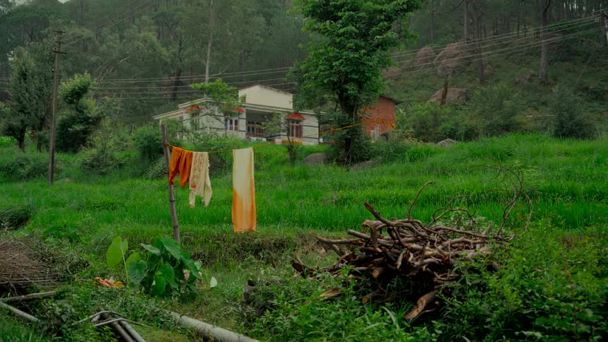Clothes hang on a line to dry in a lush green field in front of a rustic home in a rural mountain village