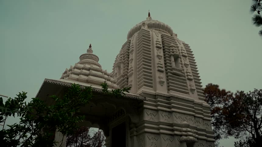A static low-angle shot of a beautiful white marble Hindu temple with intricate carvings against an overcast sky
