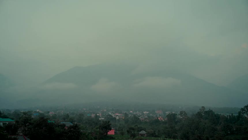 A misty mountain range looms over a quiet town in a valley on a foggy, overcast day