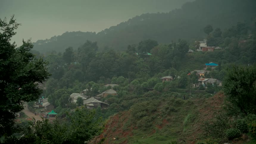 A small village is scattered across a lush green hillside on a foggy, overcast day