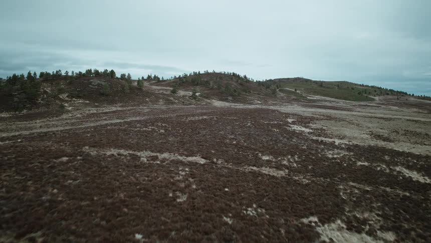 A cinematic aerial drone shot flies over a vast and desolate moorland landscape under a cloudy sky