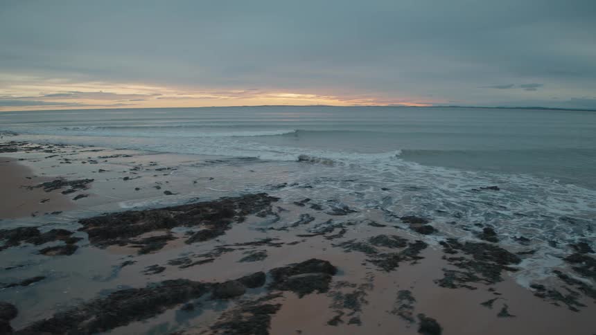 Slowly pushing in towards the gentle waves of an incoming tide on a rocky beach at dusk