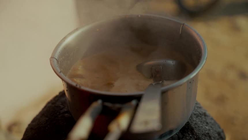 A close-up of traditional Indian Chai tea simmering in a metal pot on a rustic stove