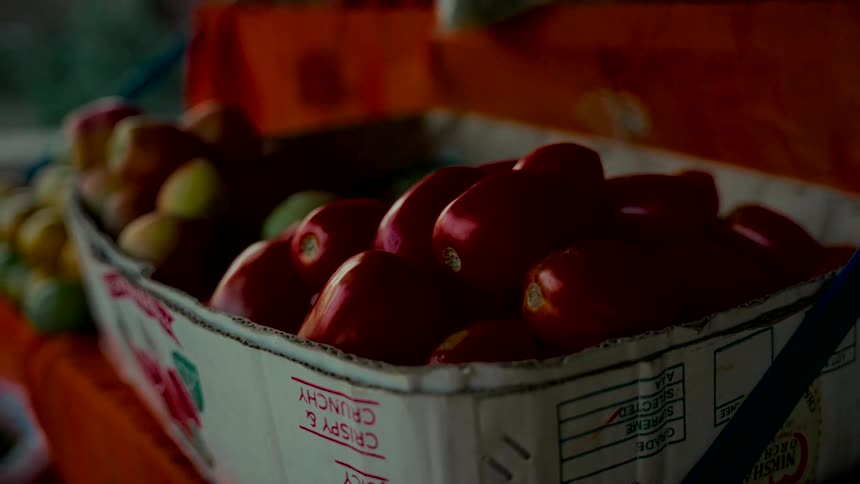 A cinematic close-up of ripe red tomatoes sitting in a cardboard box at a local street market