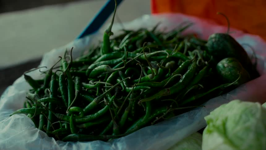 A close-up of a large pile of fresh green chili peppers in a bag at a market stall