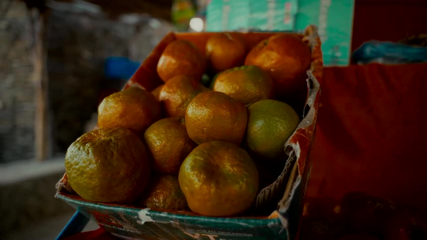 A close-up shot of a box of fresh, ripe tangerines sitting on a table at an outdoor market