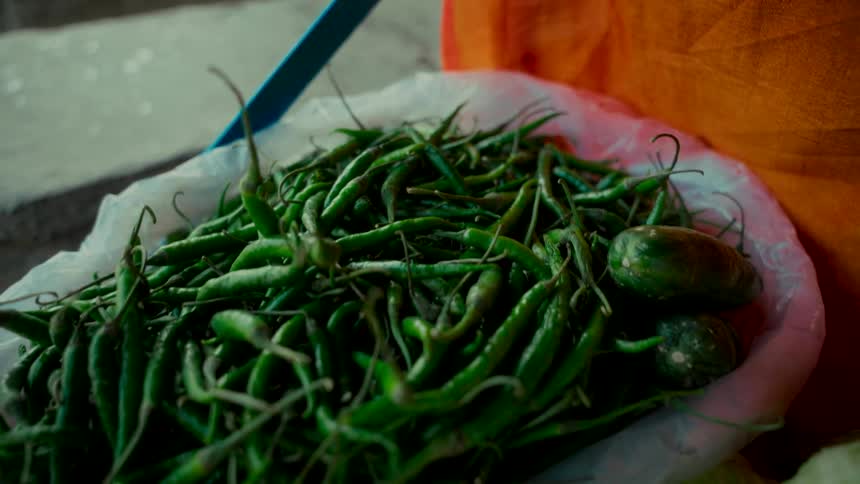 A close-up slow-motion shot reveals a plastic bag full of fresh green chili peppers at a local market stall