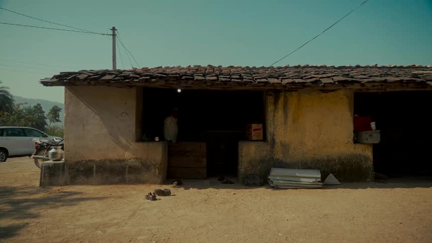 A static wide shot of a rustic roadside stall with a tile roof in a rural village in India