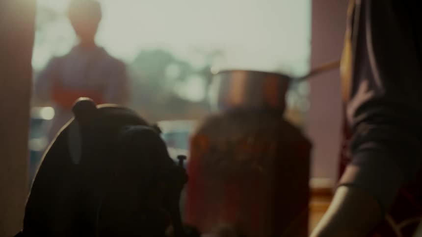 Slow motion silhouette of a person using a hand crank machine in a warm, sunlit room