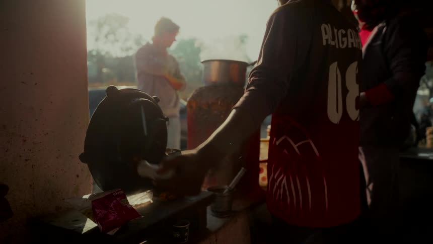 A person uses a hand-cranked air blower to stoke a fire under a steaming pot at a rustic outdoor stall