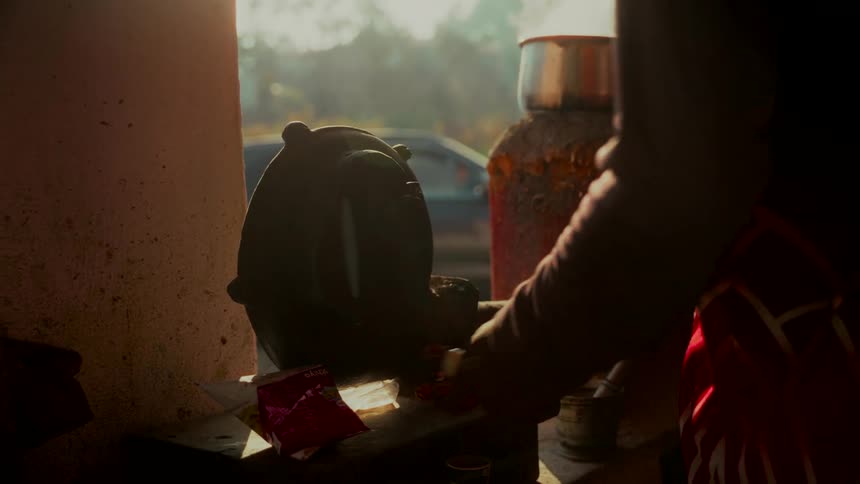 A silhouetted person hand-cranks a blower to prepare steaming hot chai tea on a traditional stove