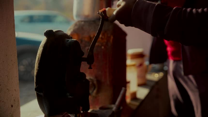 Close-up of a person using an antique manual grinder at a sunlit food stall