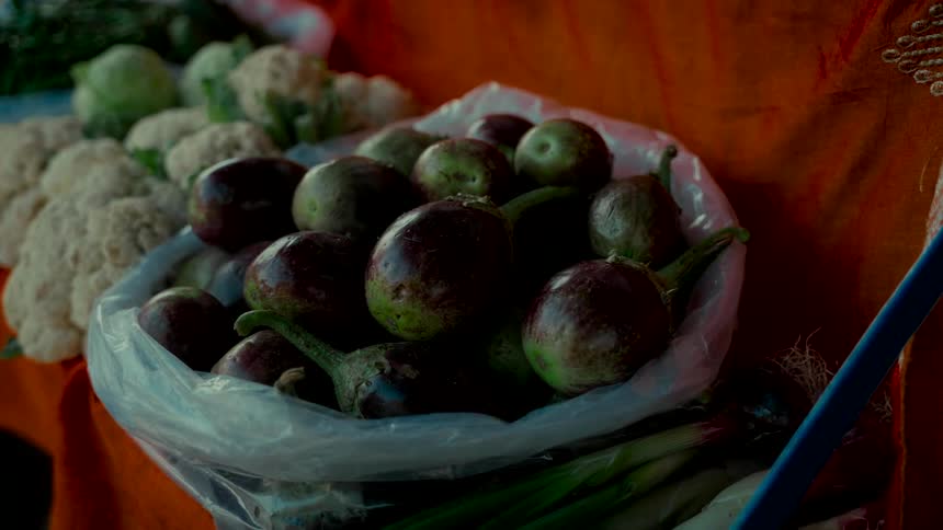 A still close-up shot of a bag of fresh purple and green eggplants at a market stall