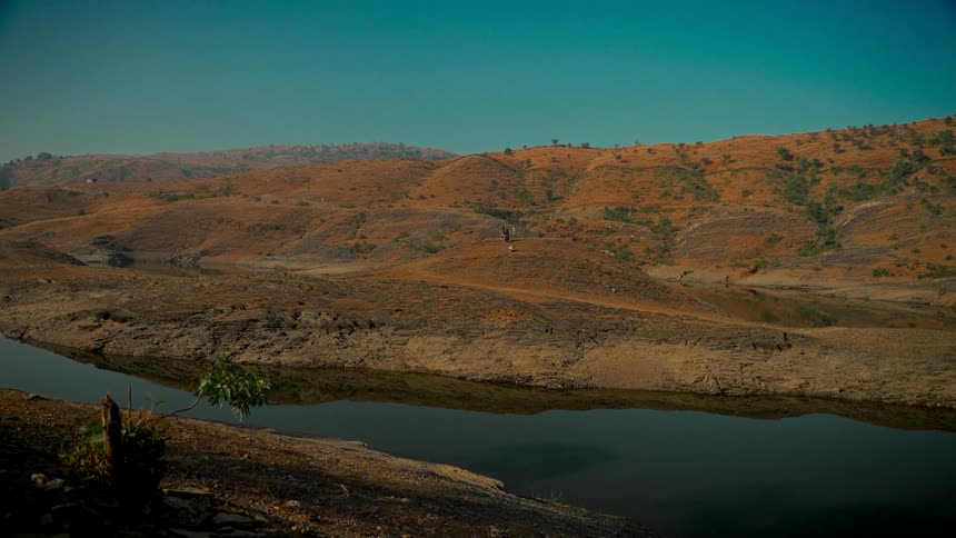 A tranquil river flows through a vast, arid landscape of orange hills under a clear teal sky