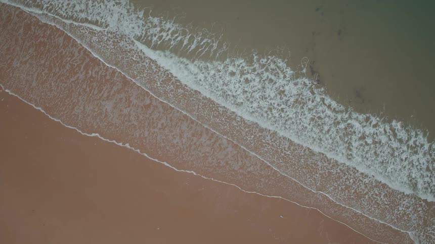 A calming top-down aerial view of gentle ocean waves lapping against a sandy shore