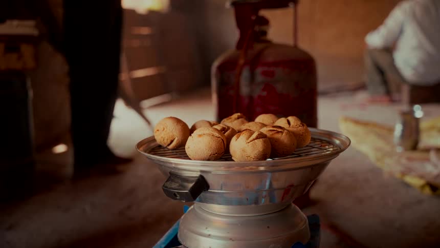 A close up of traditional Indian bread balls, litti bati, baking on a portable grill in a rustic kitchen