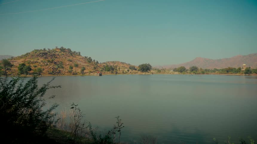 A serene view of a calm lake surrounded by arid hills under a clear blue sky