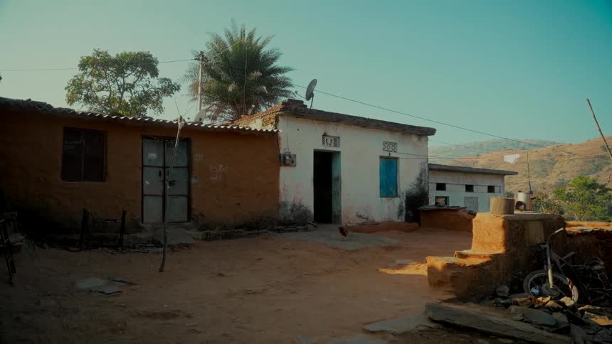 A static wide shot of humble mud and brick houses in a quiet rural Indian village on a sunny day