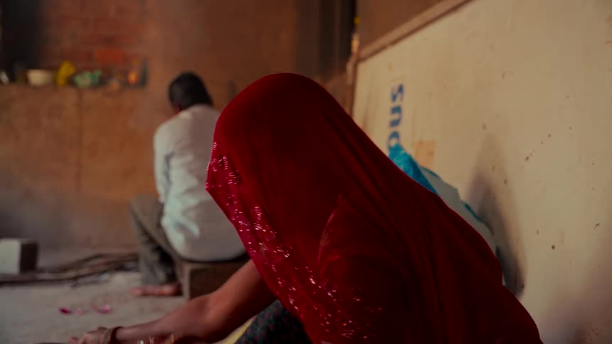 Slow motion shot of a woman in a red sparkly sari preparing food inside a village home in India