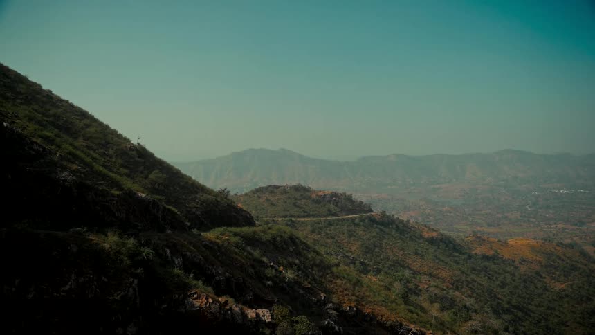 A winding mountain road snakes through a vast, arid landscape under a clear, hazy sky