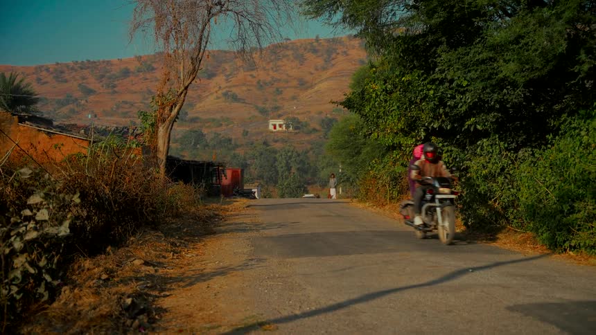 A motorcycle drives down a remote country road through a hilly, rural landscape during golden hour