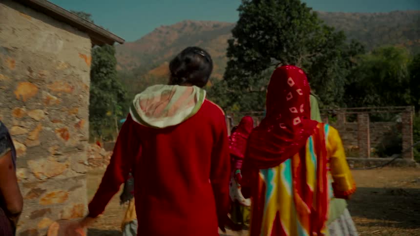 Slow motion follow shot of a group of Indian women in vibrant traditional clothing walking through a rural village in the mountains